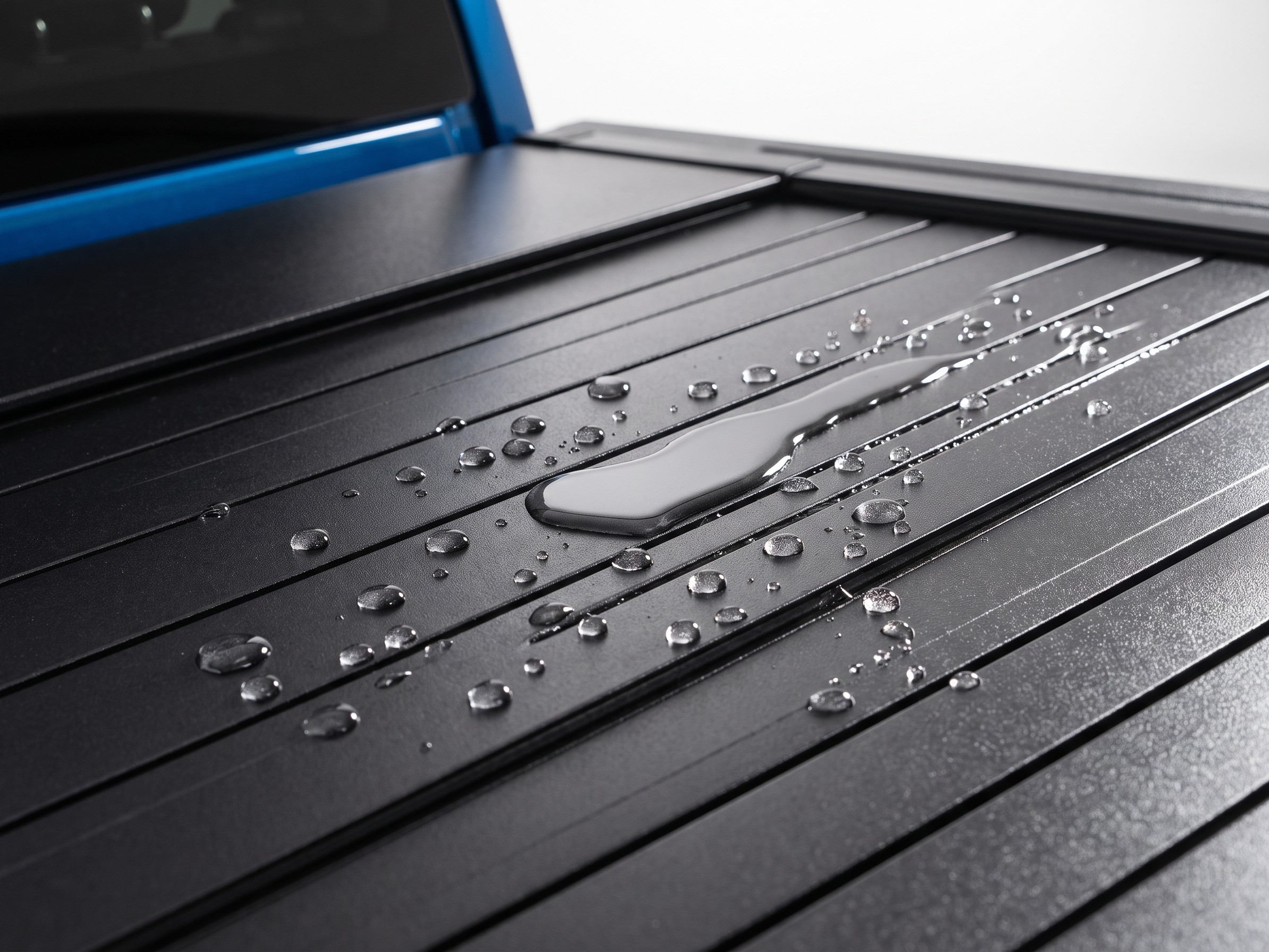 Water pooling and rolling off the sealed aluminum surface of a Coverjet tonneau cover, demonstrating weatherproofing